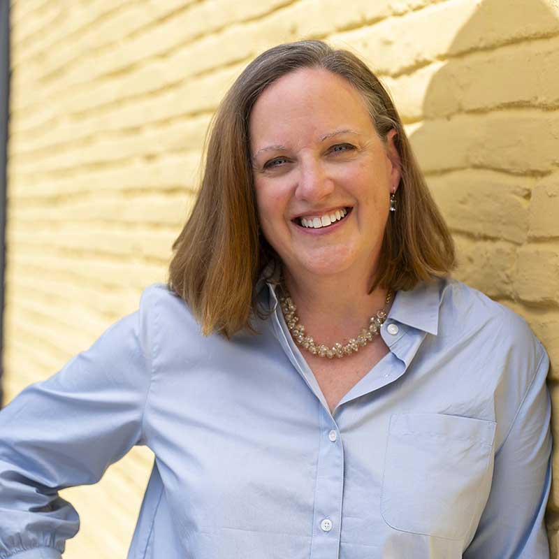 Image of Kristy Bird MaKieve leaning on a yellow wall